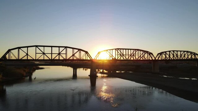 Low aerial view of a drone flying along a metal bridge with sun beams shining through with lens flare. Colorado river bridge in Parker Arizona at sunset.