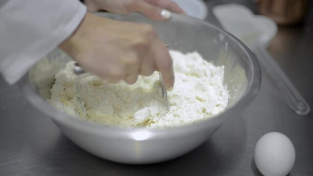 Woman chef cook baker mixing kneading dough with a metal cuter blender in a metal bowl at a local bakery restaurant in Mexico latin america