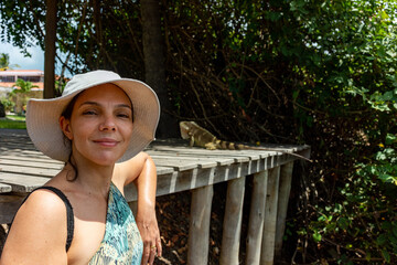 Mulher de chapéu ao ar livre com iguana passando por trás 