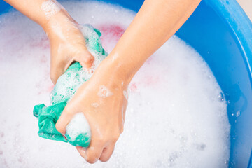 Closeup young Asian woman use hands washing color clothes in basin. Female squeeze wring out wet...