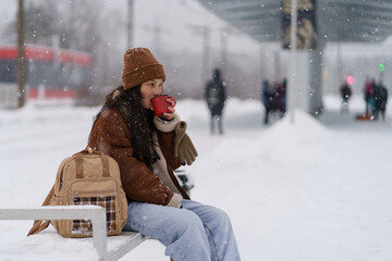 Carefree traveler girl recreating with hot tea at train station waiting for transport arrival and departure for winter vacation. Young asian woman with backpack drink coffee beverage travelling alone