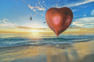 Fototapeta premium Red Heart-shaped Balloon in Front of a Beach at Sunrise