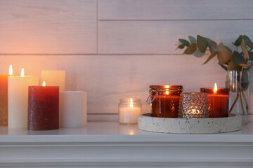 Burning candles on mantel near white wall indoors