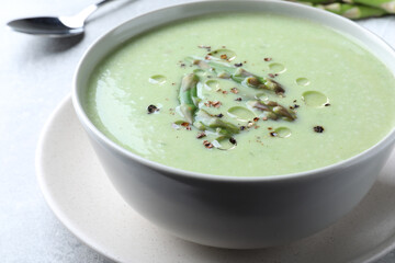 Delicious asparagus soup served on light grey table, closeup