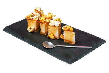 isolated on a white background cheesecake with salted caramel and popcorn on a black slate with a spoon, side view.