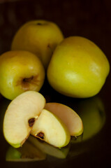 sliced slices and whole green apples with reflection on a dark background. The concept of healthy eating, diet, veganism, raw food. vertical snapshot.