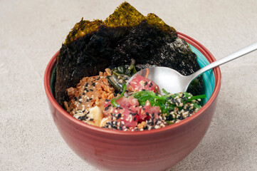 spoon with a piece of tuna in a poke salad is a traditional food of Hawaiian and Japanese cuisine in plate a side view.