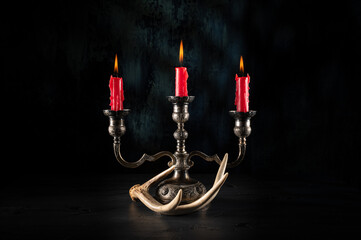 Silver candelabra, tarnished with red candles burning in a scene with antler and textured green...