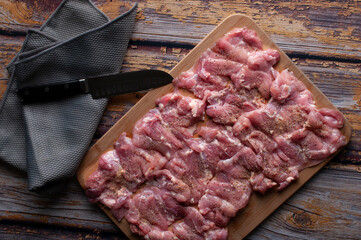 Raw chicken ready to cook with condiments like salt and pepper  with a knife and napkin on the side, on a rustic wooden table, top view, lay flat or flat lay image
