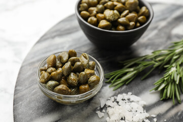 Delicious pickled capers, salt and rosemary twigs on grey marble board