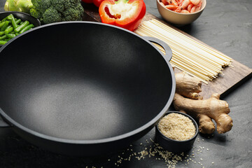 Empty iron wok and raw ingredients on black table, closeup