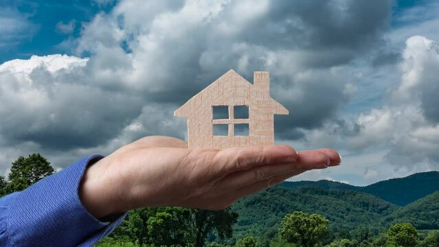 Concept of hand holding house in volatile market with time lapse sky with clouds.