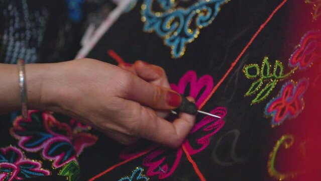 Close up of artisan's hand stitching flower embroidery onto fabric. 