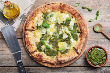 Delicious pizza with pesto, cheese and basil served on wooden table, flat lay