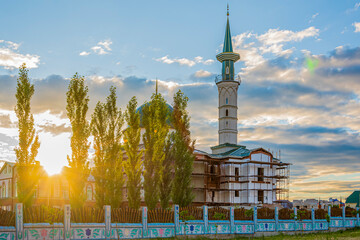 Obraz premium Building of Muslim mosque with minaret in rays of sunset against blue summer cloudy sky. Relics of Islam.
