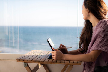 A woman is working on digital tablet on the terrace and looking at the sea