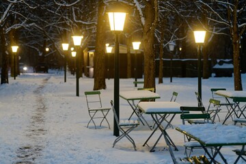 Schneebedeckte Tische und Stühle im nächtlichen Biergarten