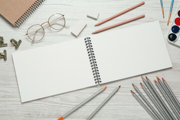Flat lay composition with blank sketchbook on white wooden table. Space for text