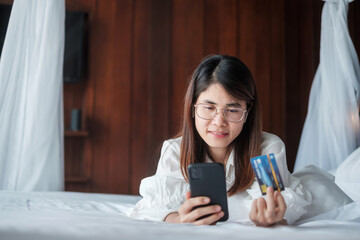 Fototapeta premium woman using mobile smart phone and credit card for online shopping while making order on bed in morning at home. technology, ecommerce, digital banking online payment and apartment living concept