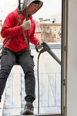 A window washer in climbing gear hangs in the window opening - 485471148