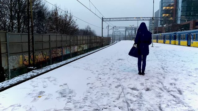 Woman from behind waiting at a train station in snowfall while a train crosses