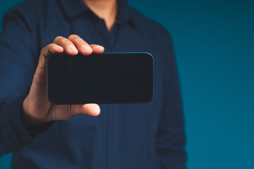 Close-up of hand man holding a blank screen mobile phone while standing on a blue background.