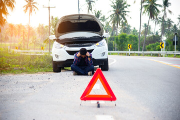 Man fixing a car problem after vehicle breakdown on the road,Traffic warning sign on road with car and driver on background