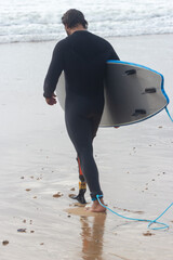 Back view of man with wavy hair walking on beach. Mid adult man with prosthetic leg in surfing suit...