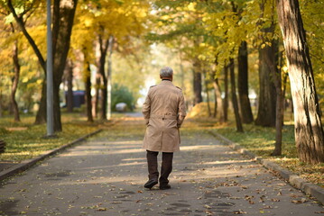 Old senior grandfather man walks away on the road in autumn