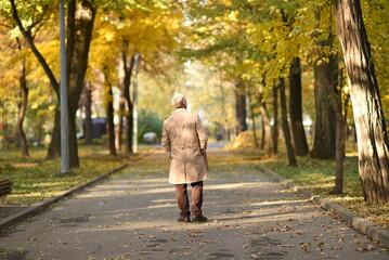 Old senior grandfather man walks away on the road in autumn