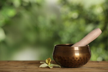 Golden singing bowl, mallet and flower on wooden table outdoors, space for text
