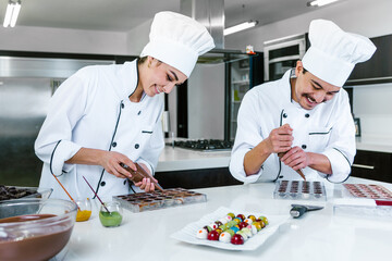 young latin couple woman and man chocolatier in chef uniform and hat preparing mexican chocolates bonbon candies at kitchen in Mexico Latin America