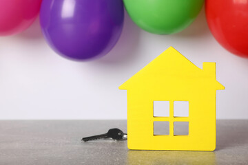 Yellow house model with key and balloons on grey table, space for text. Housewarming party