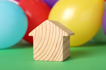 Wooden house model and balloons on green background. Housewarming party