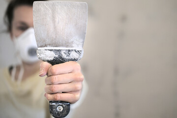 Dirty putty knife with cocnrete close-up in the hand of a woman with respirator on the face making home repairs