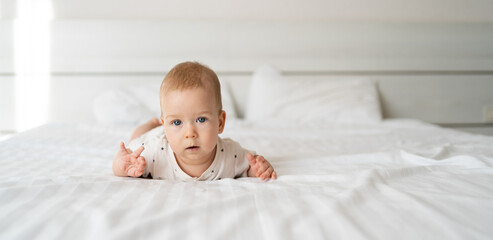 serious white caucasian baby boy with blue eyes six months old lying on the bed and looking at the camera. straight view. childhood happy lifestyle