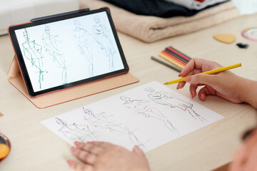 Designer watching tutorial how to draw fashion sketches on tablet computer at her workplace