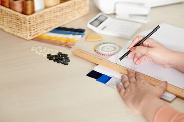 Hands of tailor drawing technical sketch of clothing item for customer