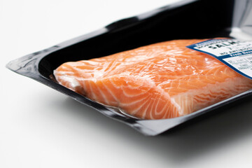 Closeup of fresh farmed Atlantic salmon fillet in orange color with clear white veins in a vacuum sealed plastic container isolated on a white background.