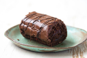 Delicious chocolate roll cake in ceramic plate on white wooden background, close up .Drunk cherry cake