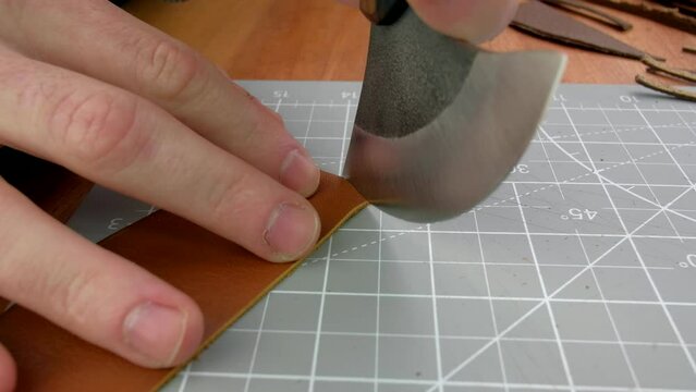 Close up hands tanner cuts special halberd cutting knife leather piece in workshop. Craft production.