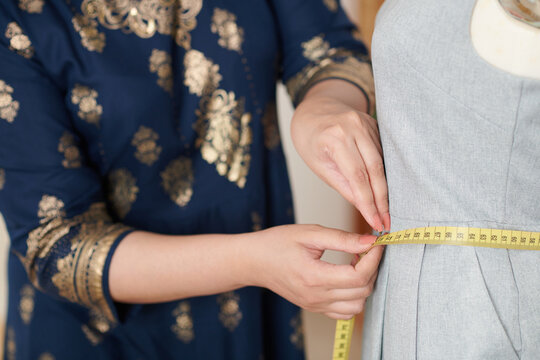 Closeup image of tailor measuring waist of dress on mannequin with measuring tape