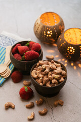 Strawberries and cashews served in a coconut made bowl next to coconut made candle holders on a grey background with wooden spoons and blue napkin