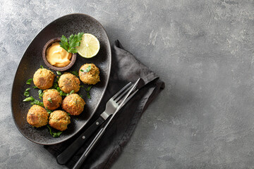 Chickpea falafel with sauce on black plate and grey background top view, copy space for text