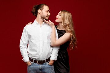A lovely couple, a pretty woman with blond hair and a handsome man posing in the red background