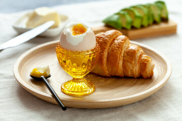 French breakfast with croissant, avocado, soft egg and butter, close-up