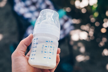 Close up of hand holding a nursing infant milk bottle with labels of measurement. Personal...