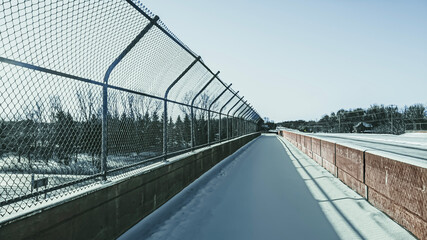Sidewalk over the highway covered in snow with chain-link fence and concrete barricade