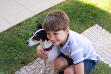 Cute little boy hugging dog. Schoolboy in T-shirt and shorts and white puppy on summer day. Pet,...