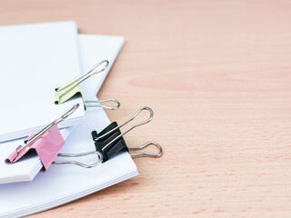 Image of binder clips with blank white paper on wooden table.
